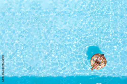 Woman on a donut buoy in a blue water swimming pool aerial view from above