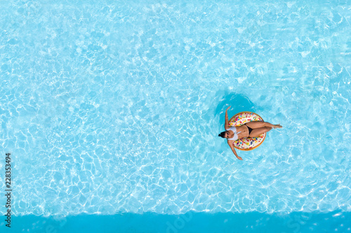 Woman on a donut buoy in a blue water swimming pool aerial view from above