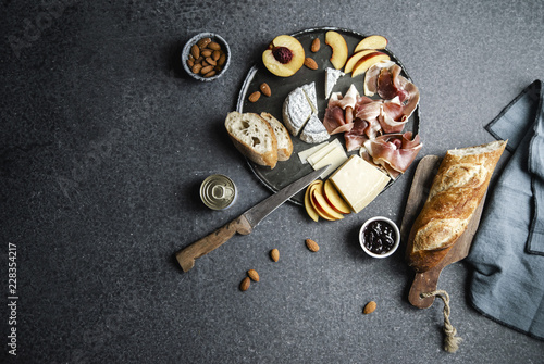 Cheese and ham plate with parmesan, camamber, goat cheese, ham, baguette and snacks. Overhead view, dark background photo