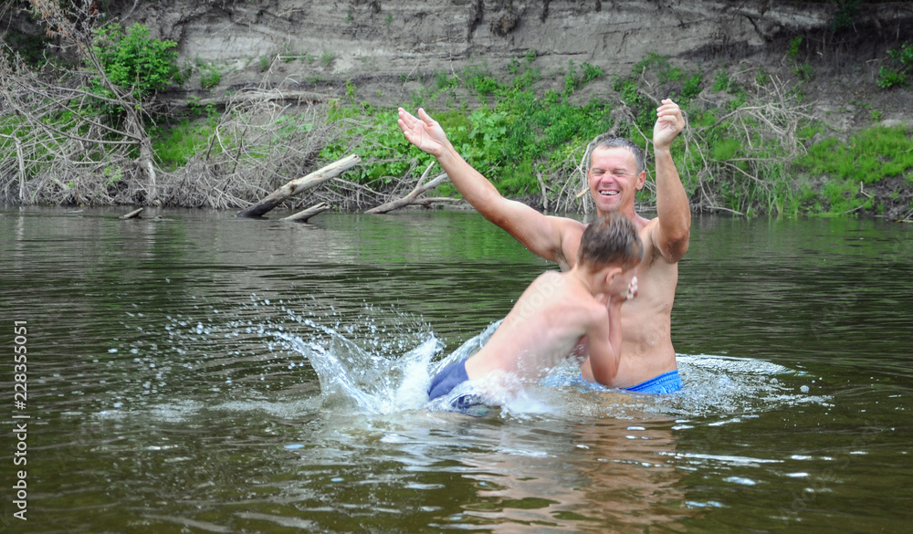 Fototapeta premium Father throws his son in the water, play, fun family vacation. jumps, swims and splashes in the river.