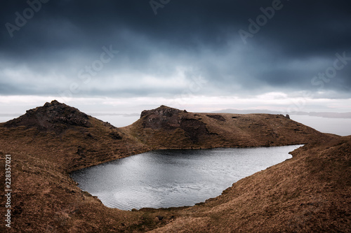 Jezioro otoczone brązowymi górami z nadciągającymi ciemnymi chmurami