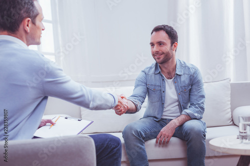 Gratitude. Pleased positive bearded man shaking hands with professional psychiatrist while being extremely thankful to him for a high quality assistance photo