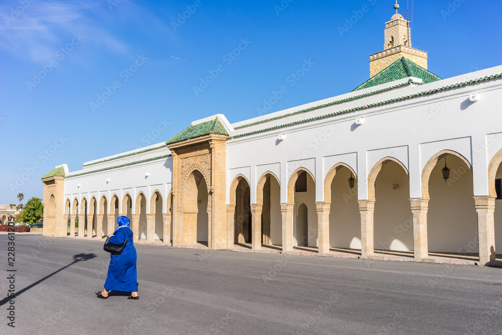 Obraz premium Woman walking by the small mosque in the mechouar. Located at a large parade ground attached to the Dar-al-Makhzen which is the primary and official residence of the king of Morocco in Rabat.