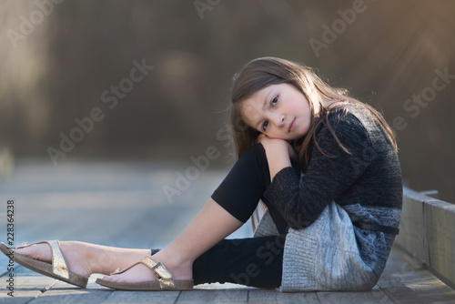 Canvas Print Young girl with long brown hair and a sweater dress posing on a wooden pathway