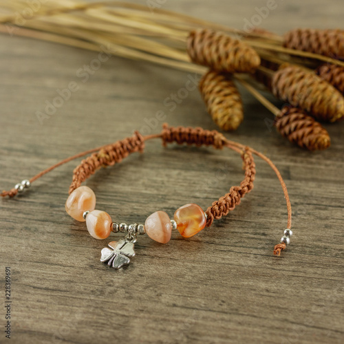 Charm brown bracelet on wooden background and dry flowers