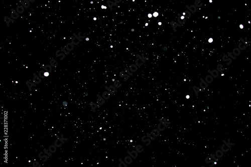 Snowstorm texture. Bokeh lights on black background, shot of flying snowflakes in the air © donikz