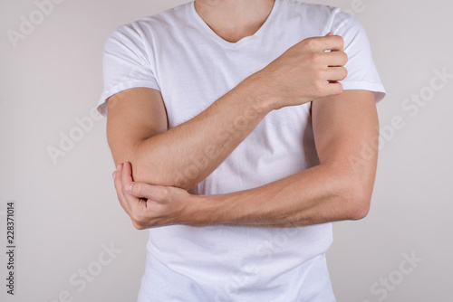 Cropped close up photo portrait of unhappy upset sad guy holding touching painful elbow wearing white t-shirt isolated grey background copy space photo