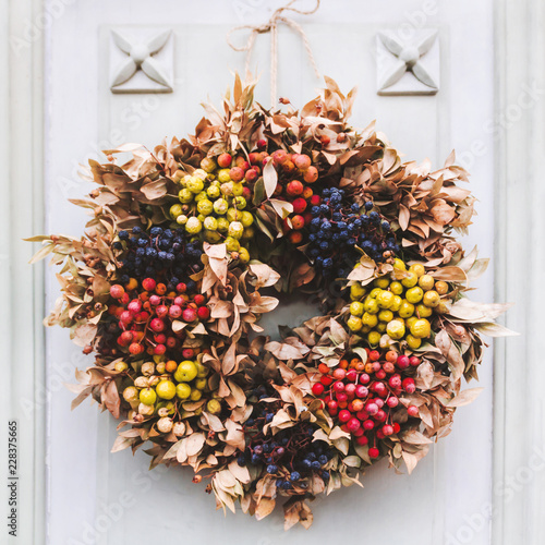 Wreath of dried berries and leaves on wooden door of house.