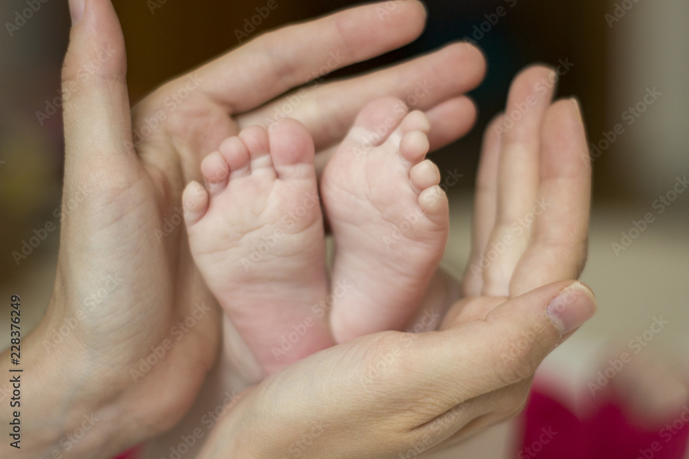 Closeup of small feet of newborn in caring loving mother's hands
