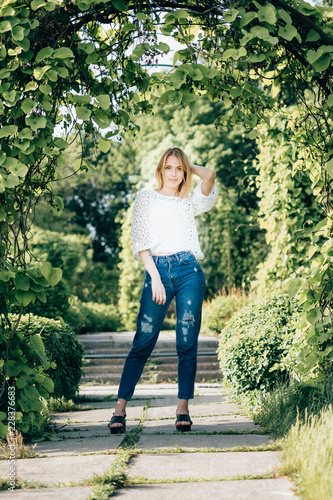 Beautiful attractive young woman posing in spring park wearing white knitted top and blue jeans, modern creative toning