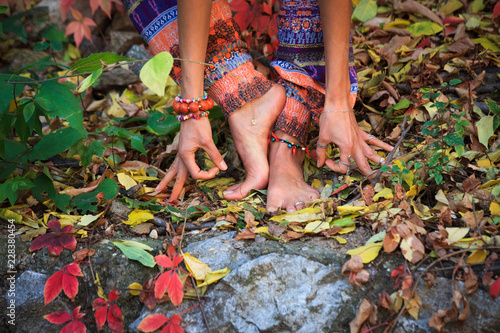 barefoot woman legs and hands in yoga and mudra gesture in colorful autumn leaves outdoor