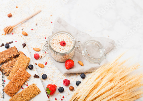 Organic cereal granola bar with berries on marble board with honey spoon and jar of oats and linen towel on marble background. Raw wheat bundle photo