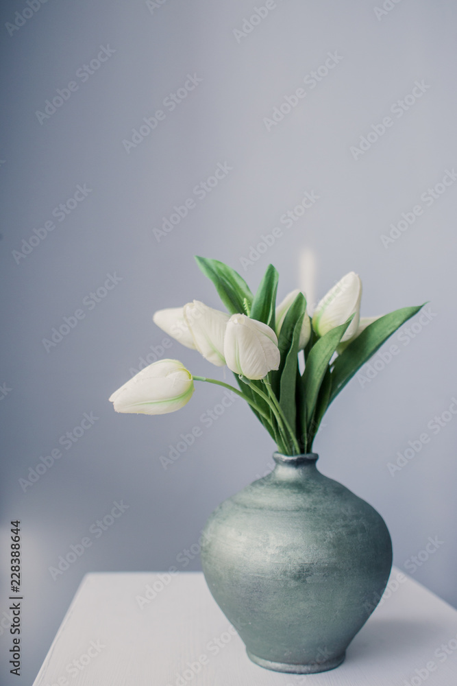 White tulips in a jug on a table in the early morning in a room with gray walls