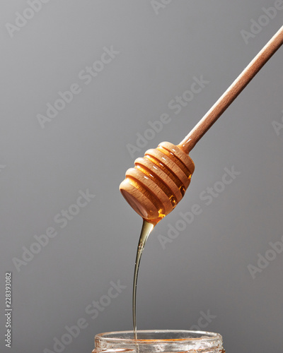 Close up of wooden stick with dripping sweet natural honey on a gray background, traditional useful sweetness.
