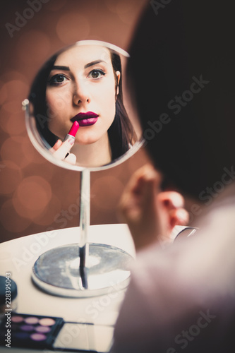 portrait of the beautiful young woman doing her make-up and looking in the mirror