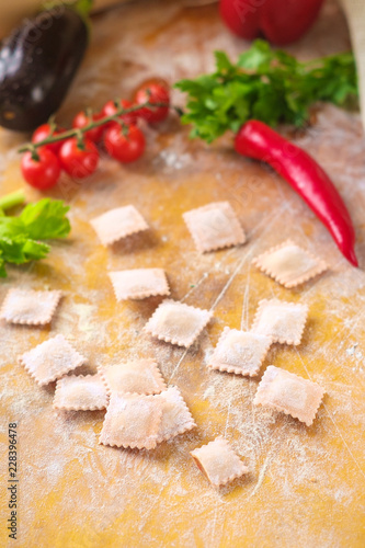 raw colored ravioli ravioli in flour with vegetables and tomatoes on wooden background. Process of making italian pasta