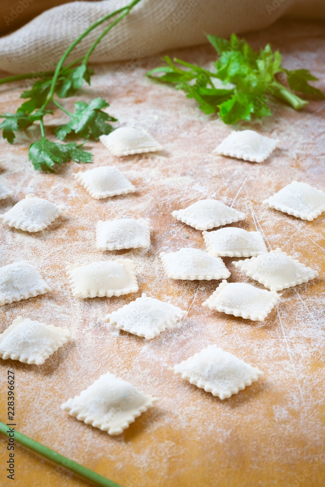 traditional white uncooked ravioli with cheese on a cutting board with flour, handmade, on a wooden table. cooking process traditional white uncooked ravioli with cheese on a cutting board with flour, handmade, on a wooden table. cooking process