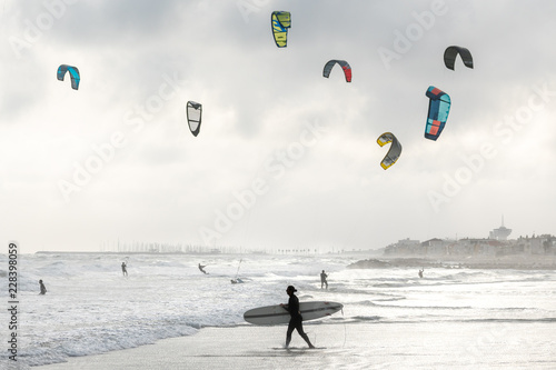 un surfer passe devant des kitesurf sous un ciel nuageux