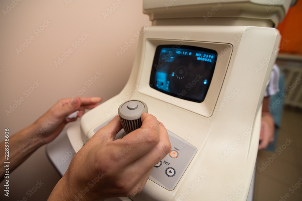 The doctor's hands control the apparatus for testing the vision behind which the patient is sitting The doctor's hands control the apparatus for testing the vision behind which the patient is sitting
