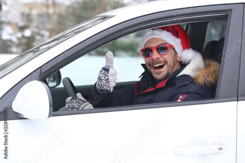 Close up portrait of car driver with santa hat and thumb up enjoying the snow and sunny dan.