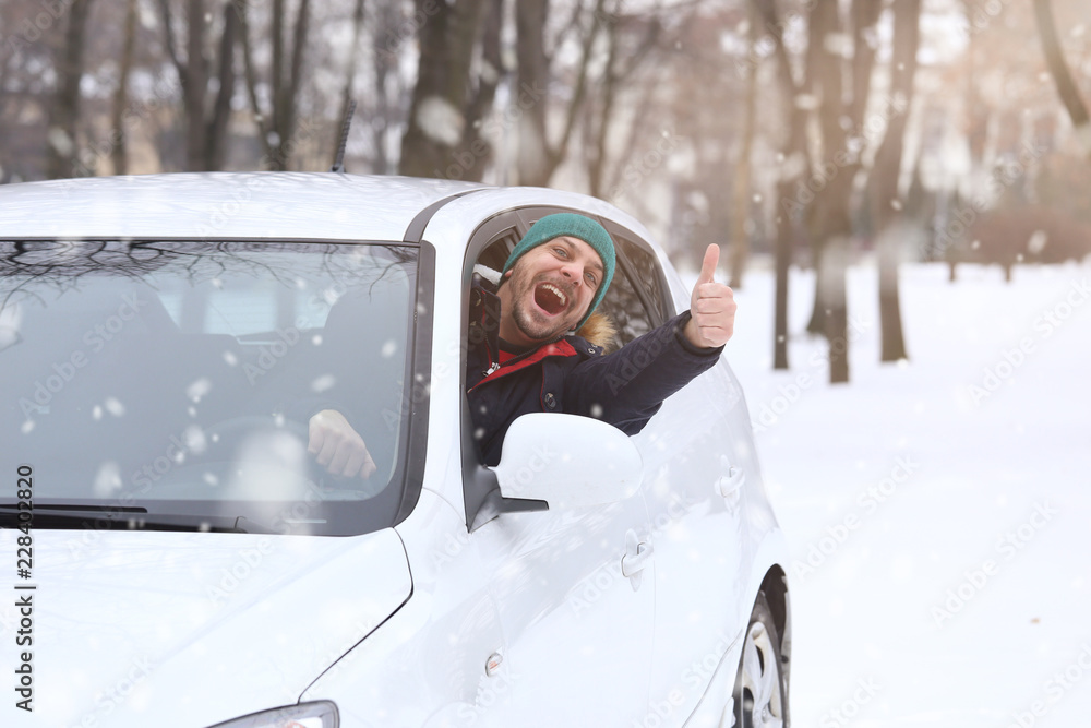 Portrait of car  driver with smile santa hat and thumb up through car window. On the road winter holidays concept.