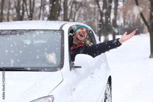 Portrait of car driver with santa hat through car window enjoying the snowy day. On the road winter vacation and holidays concept.