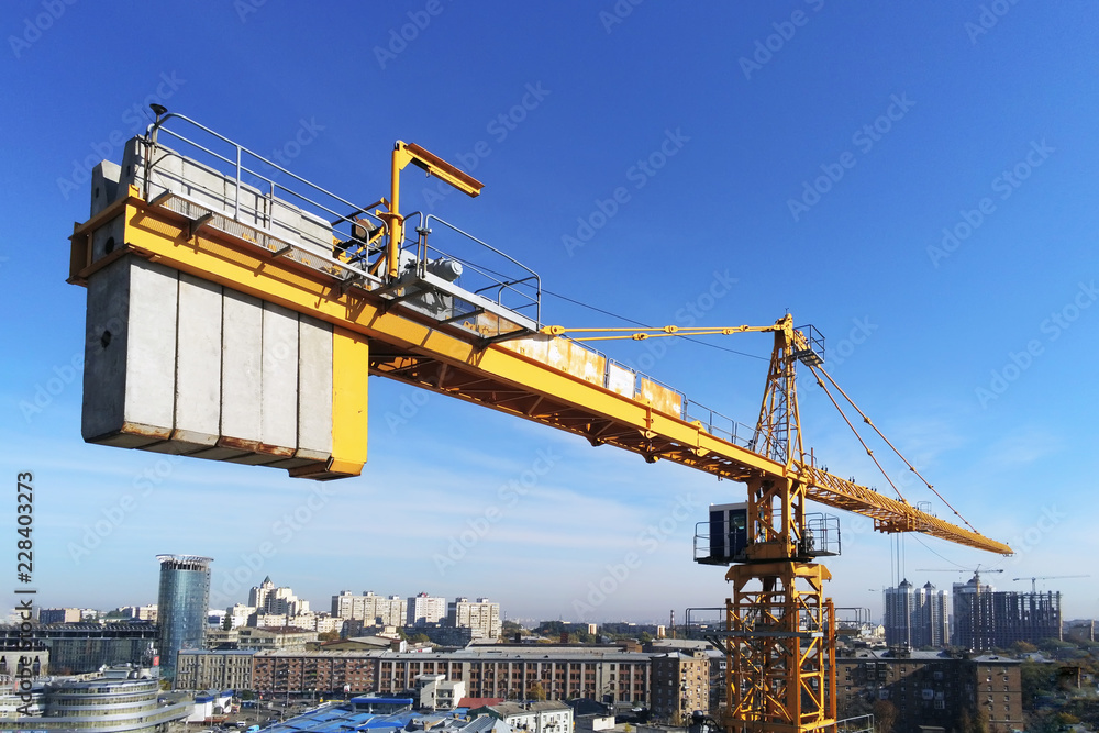 High building construction site. Big industrial tower crane with blue sky amd cityscape on background. Concrete plates weight balance. Counterweight. Aerial drone view. Metropolis city development