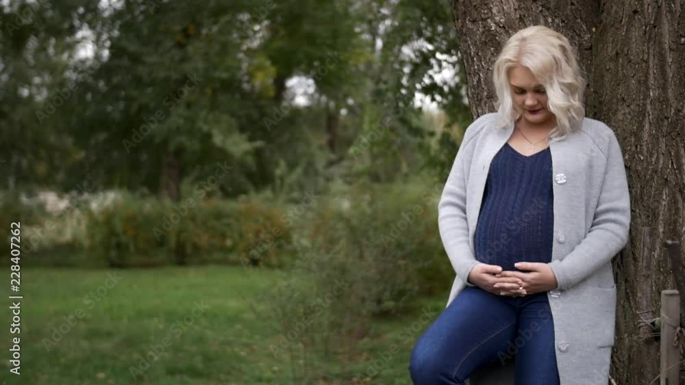 HD Pregnant woman standing next to tha tree and looks at her belly HD Pregnant woman standing next to tha tree and looks at her belly