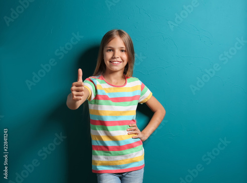 Smiling little girl in t-shirt showing thumb-up on color background