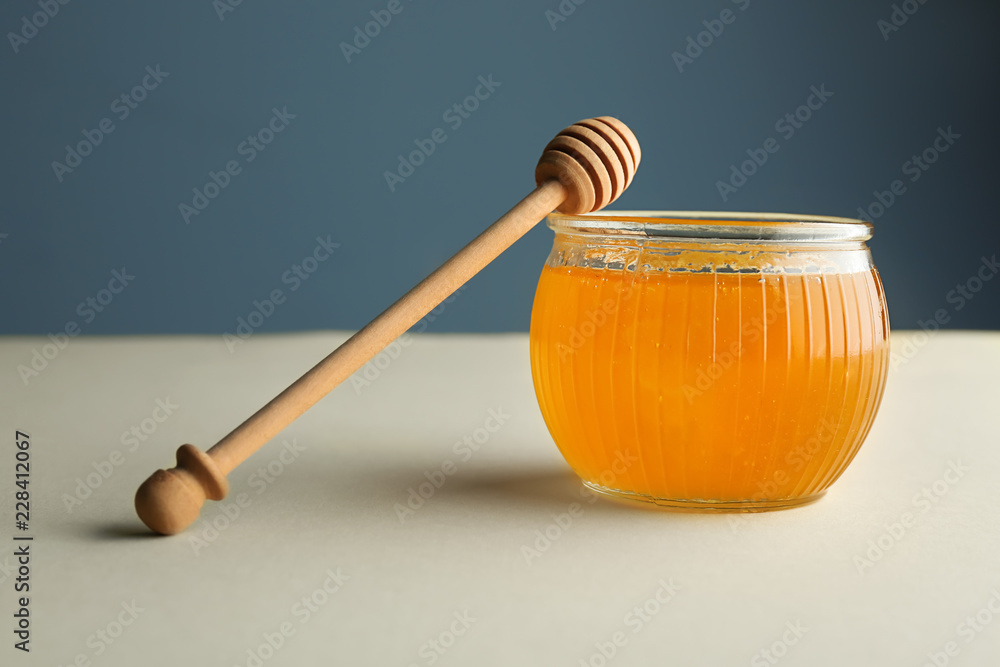 Glass jar full of honey and dipper on light table Glass jar full of honey and dipper on light table