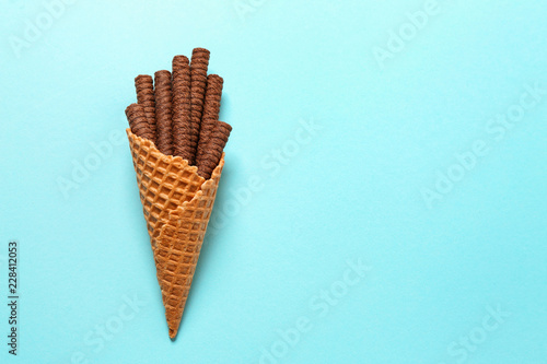 Waffle cone with chocolate wafer sticks on color background