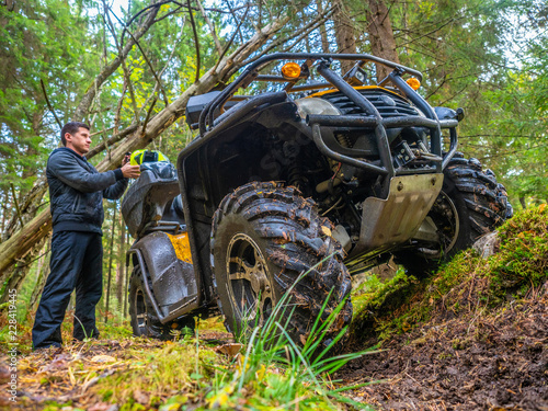 A man travels in an all-terrain vehicle. Forest. ATV. Leisure. A man goes on the road on the ATV. The traveler takes off his helmet. Off-road.