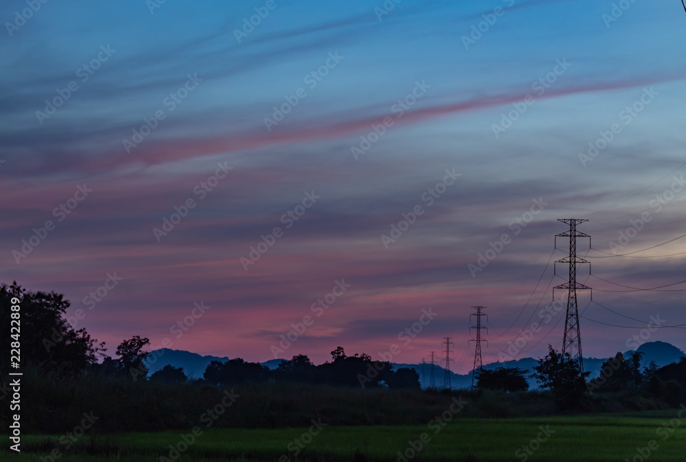 The light of sunset behind the mountain and the high voltage poles.
