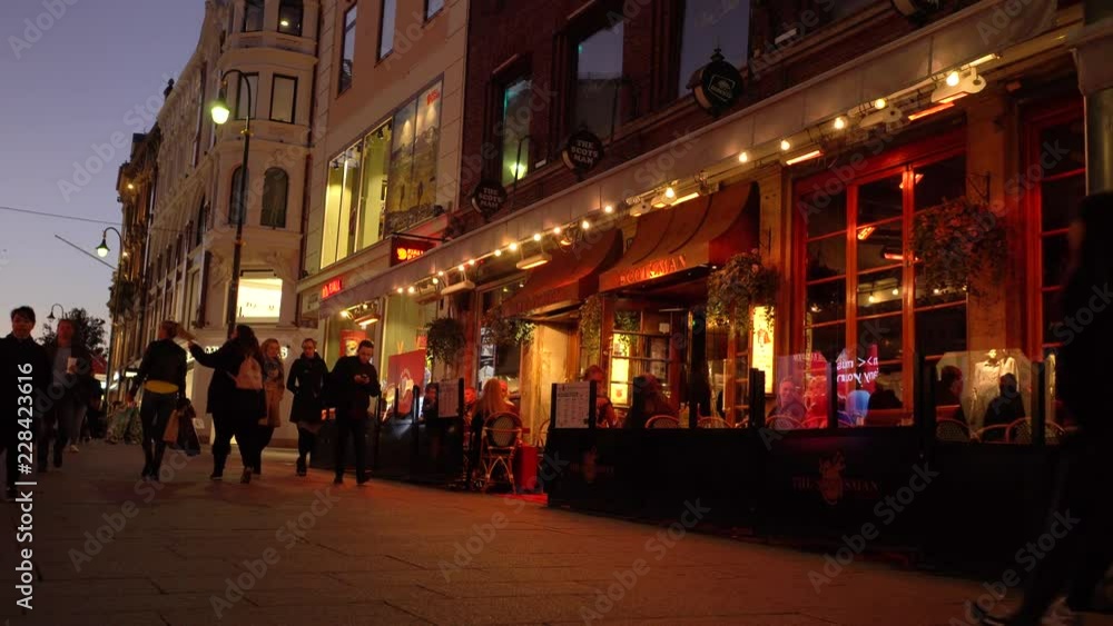 Evening dusk reddish color city street with restaurant and people having a dinner and pedestrians passing by