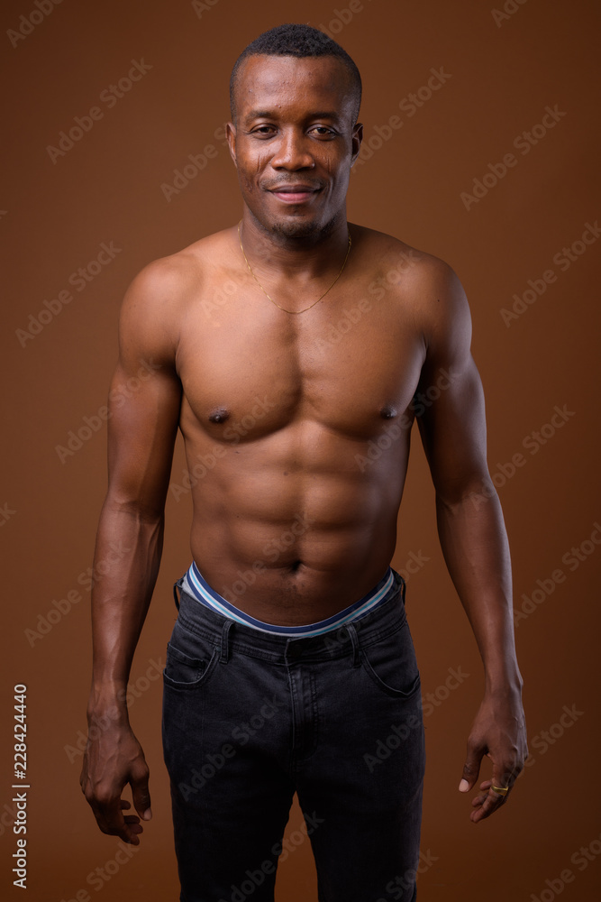 Fototapeta premium Young shirtless African man against brown background