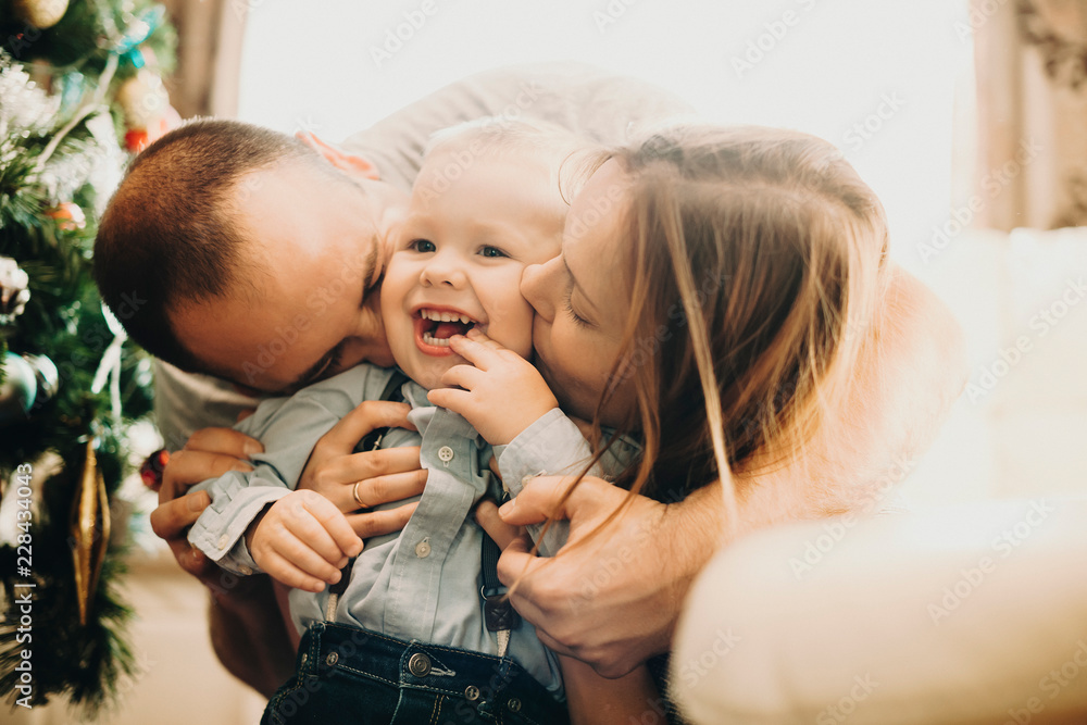 Parents kissing adorable toddler in cheeks - obrazy, fototapety, plakaty 