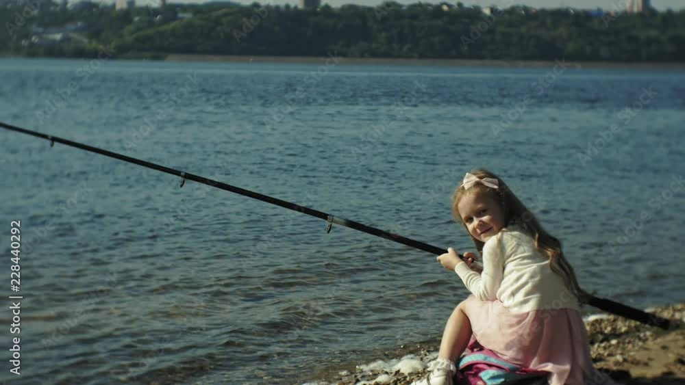 Cute little girl is playing with a fishing rod on a fishing boat near the river Cute little girl is playing with a fishing rod on a fishing boat near the river