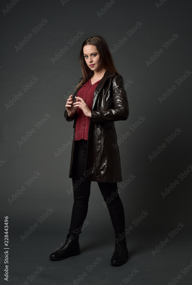 full length portrait of brunette girl wearing long leather coat and boots. standing pose on grey studio background. full length portrait of brunette girl wearing long leather coat and boots. standing pose on grey studio background.