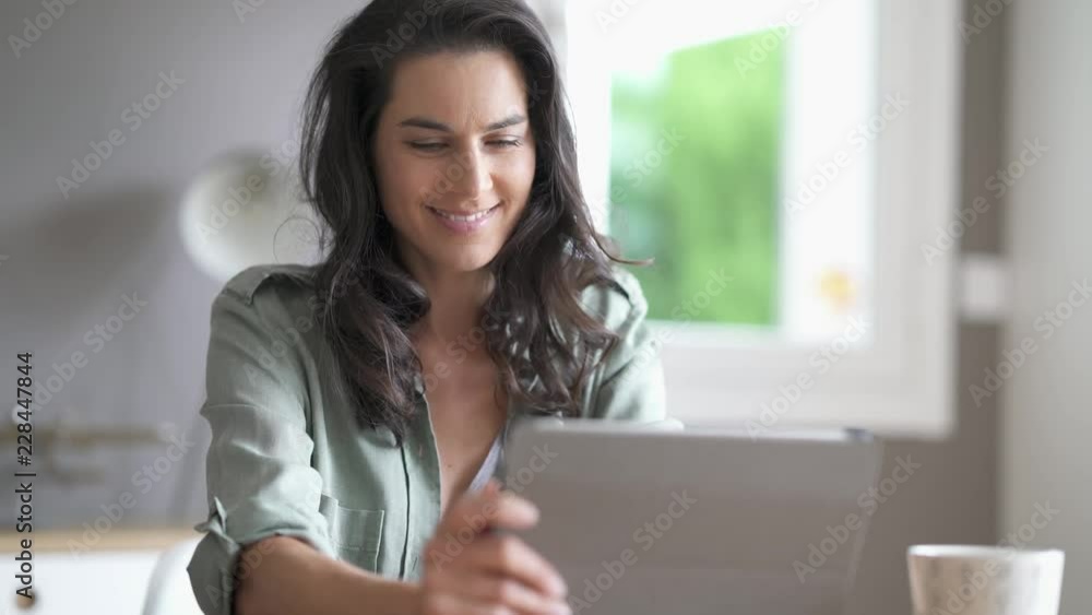 Brunette woman sitting at a table looking at her tablet Brunette woman sitting at a table looking at her tablet
