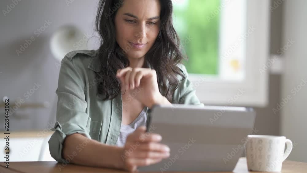 Brunette woman sitting at a table looking at her tablet Brunette woman sitting at a table looking at her tablet