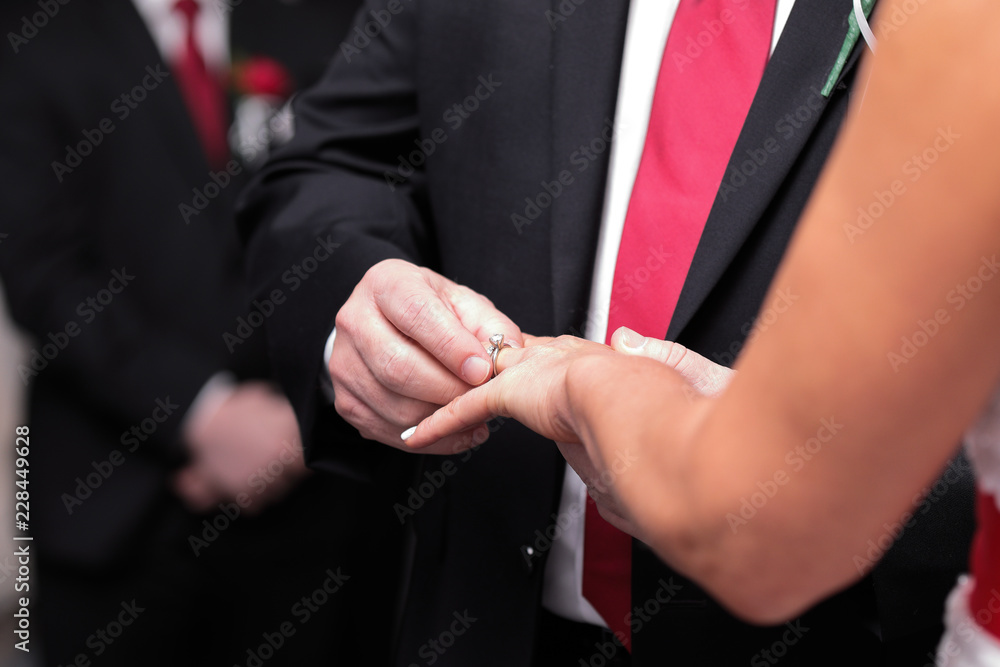Groom putting ring on bride's finger during wedding ceremony