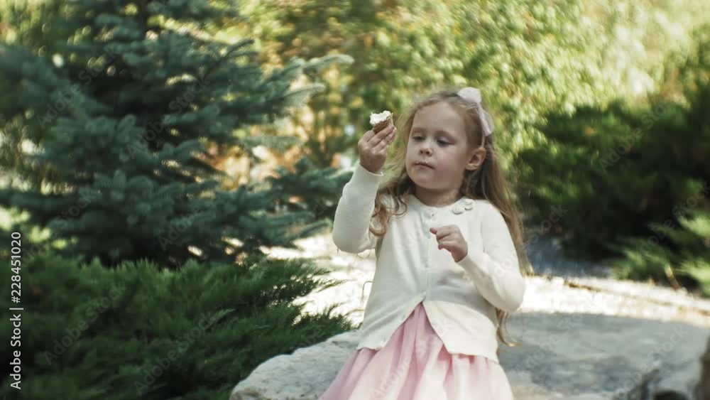A cute girl is sitting in the park and eating ice cream A cute girl is sitting in the park and eating ice cream