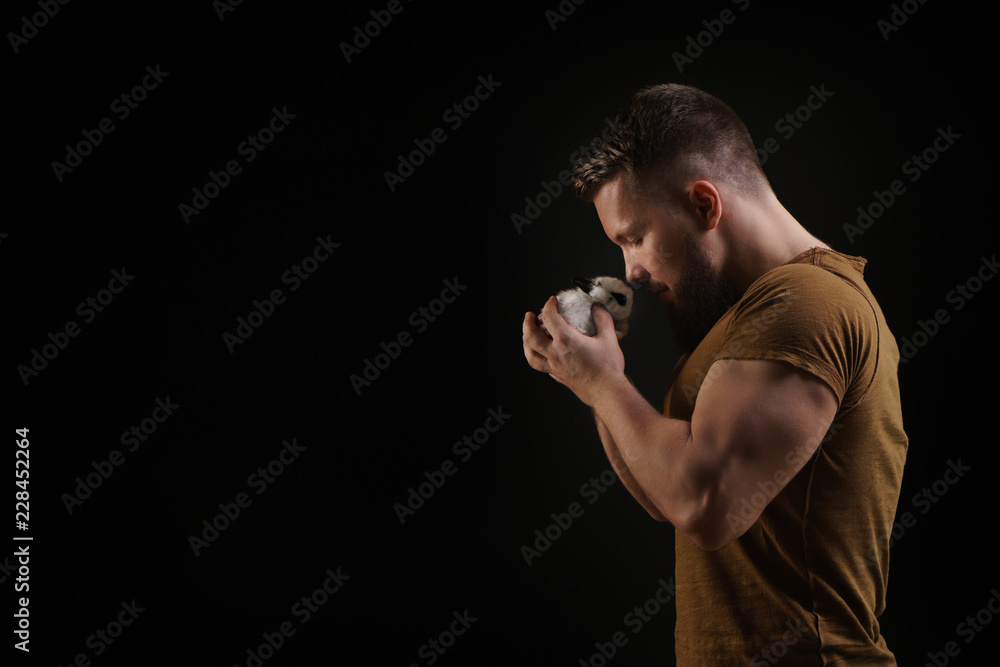 Bodybuilder with a little rabbit. Muscular man with a beard in a tight T-shirt holding a pet. Stylish and sporty young man loves his pet.