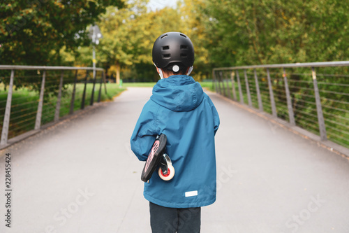 Kind mit Helm und Waveboard Skateboard unter dem Arm Hand haltent im Park beim spielen photo