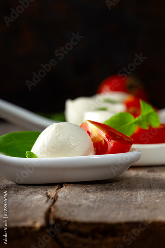 Spoons with mozzarella cheese balls, cherry tomato and basil on wooden background