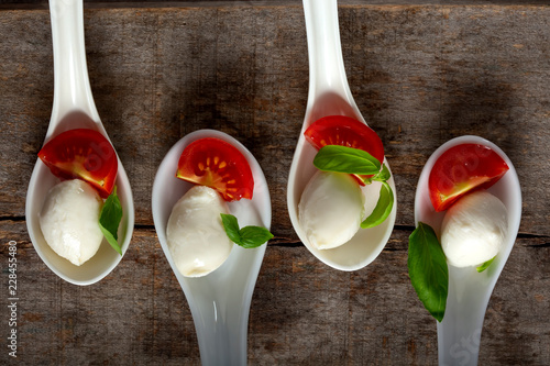 Spoons with mozzarella cheese balls, cherry tomato and basil on wooden background