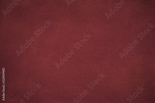 Background of dark red suede fabric closeup. Velvet matt texture of wine nubuck textile with gradient.