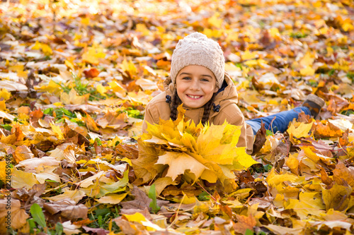 Autumn portrait  Cute smiling little girl lying on the fallen leaves and holding the bouquet of yellow maple leaves in her hands