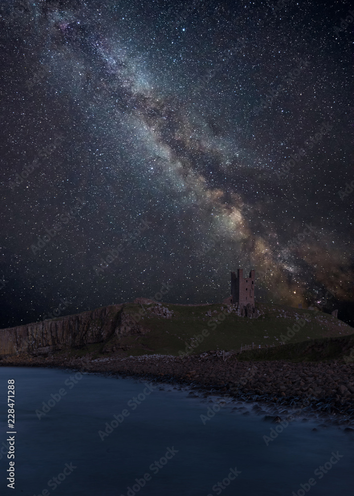 Vibrant Milky Way composite image over landscape of Dunstanburgh Castle on Northumberland coastline in England