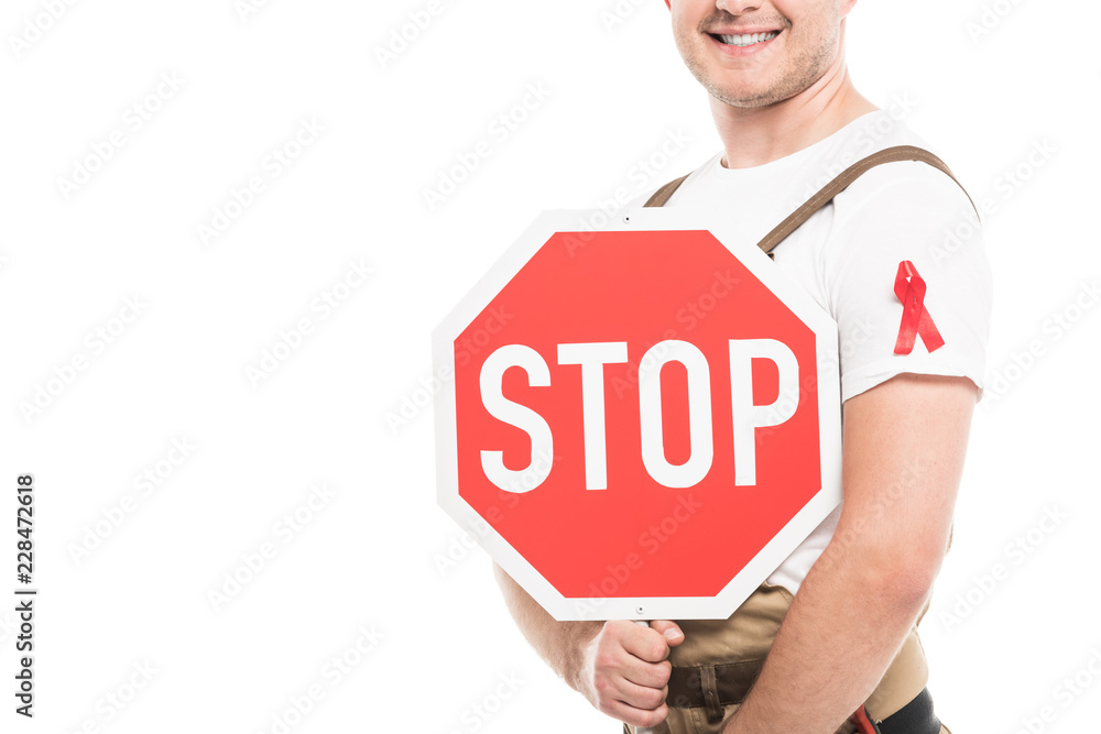 cropped shot of smiling builder with aids awareness red ribbon on overall holding stop road sign isolated on white cropped shot of smiling builder with aids awareness red ribbon on overall holding stop road sign isolated on white